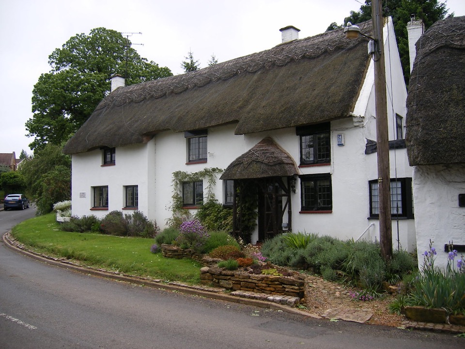 A white rendered cottage under a thatched roof with a thatched porch at Coton in Northamptonshire