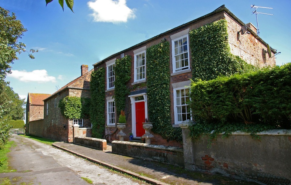 A brick farmhouse with sash windows and a red front door, half covered in ivy, on a lane in Lincolnshire