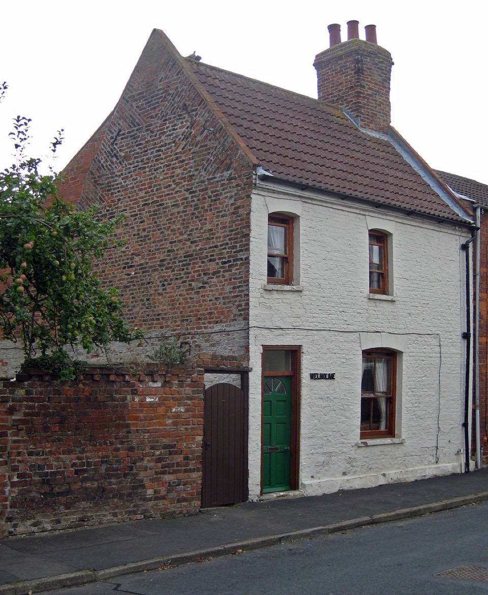 A white painted brick cottage with a green front door beside an exposed red brick gable in Lincolnshire